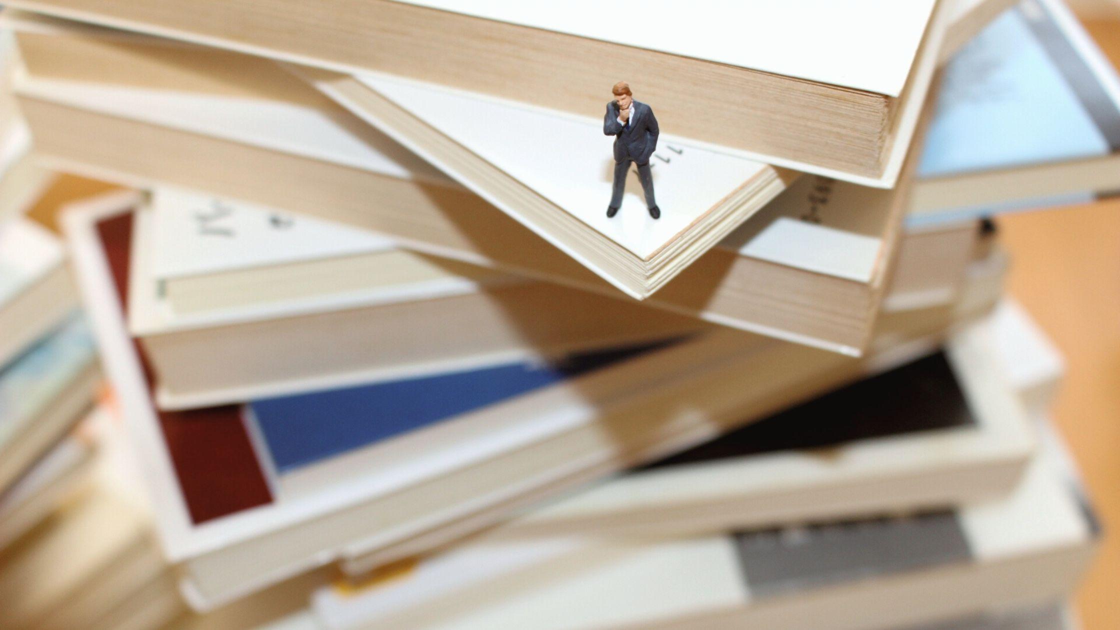 積まれた本の上に立つミニチュア男性